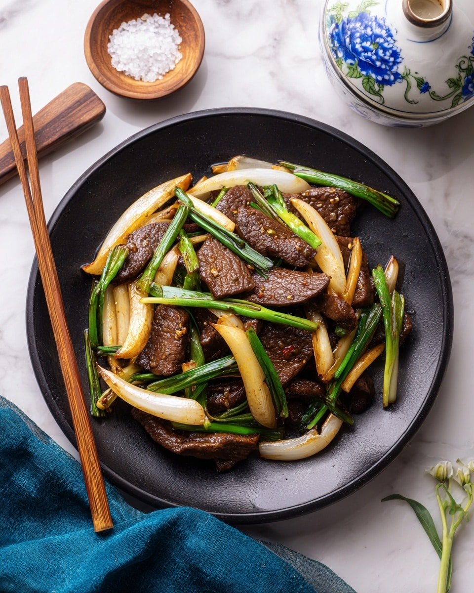 A black plate holds stir-fried slices of dark brown liver staggered with thick, curved pieces of lightly cooked white onion and long, green chive stalks scattered on top. The liver pieces are shiny and moist with a warm brown glaze, while the onions have a slight golden tint from cooking. Thin wooden chopsticks rest on the left edge of the plate. The plate sits on a white marbled surface with a small wooden bowl of coarse salt and a white ceramic container with blue floral designs blurred in the background on the top side. A blue cloth is casually placed in the lower right corner of the image. photo taken with an iphone --ar 4:5 --v 7 — Pork Liver Stir Fry, stir fry with liver, quick liver recipe, savory liver dish, Asian liver stir fry